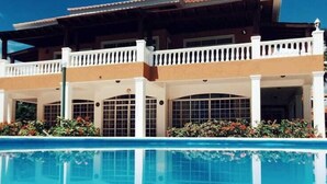 A hotel with a swimming pool, a covered patio, and a clear blue sky. - 9th Hole Villa (Guayacanes)