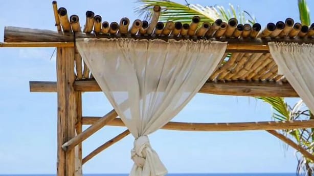 A wooden beach cabana with a bench and a table set for a meal, overlooking the ocean. - 9th Hole Villa (Guayacanes)