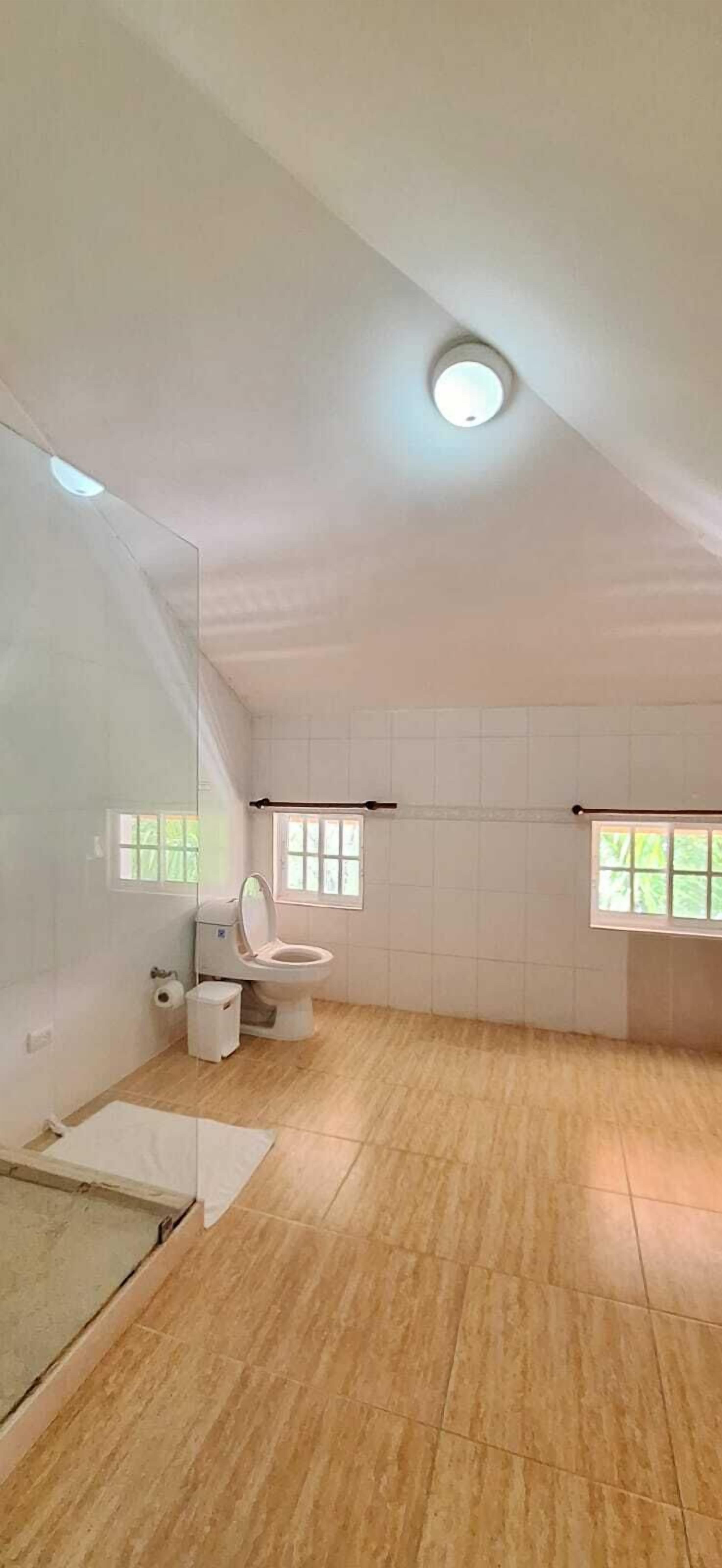 Ett rymligt badrum med en toalett, en liten papperskorg och ett fönster.