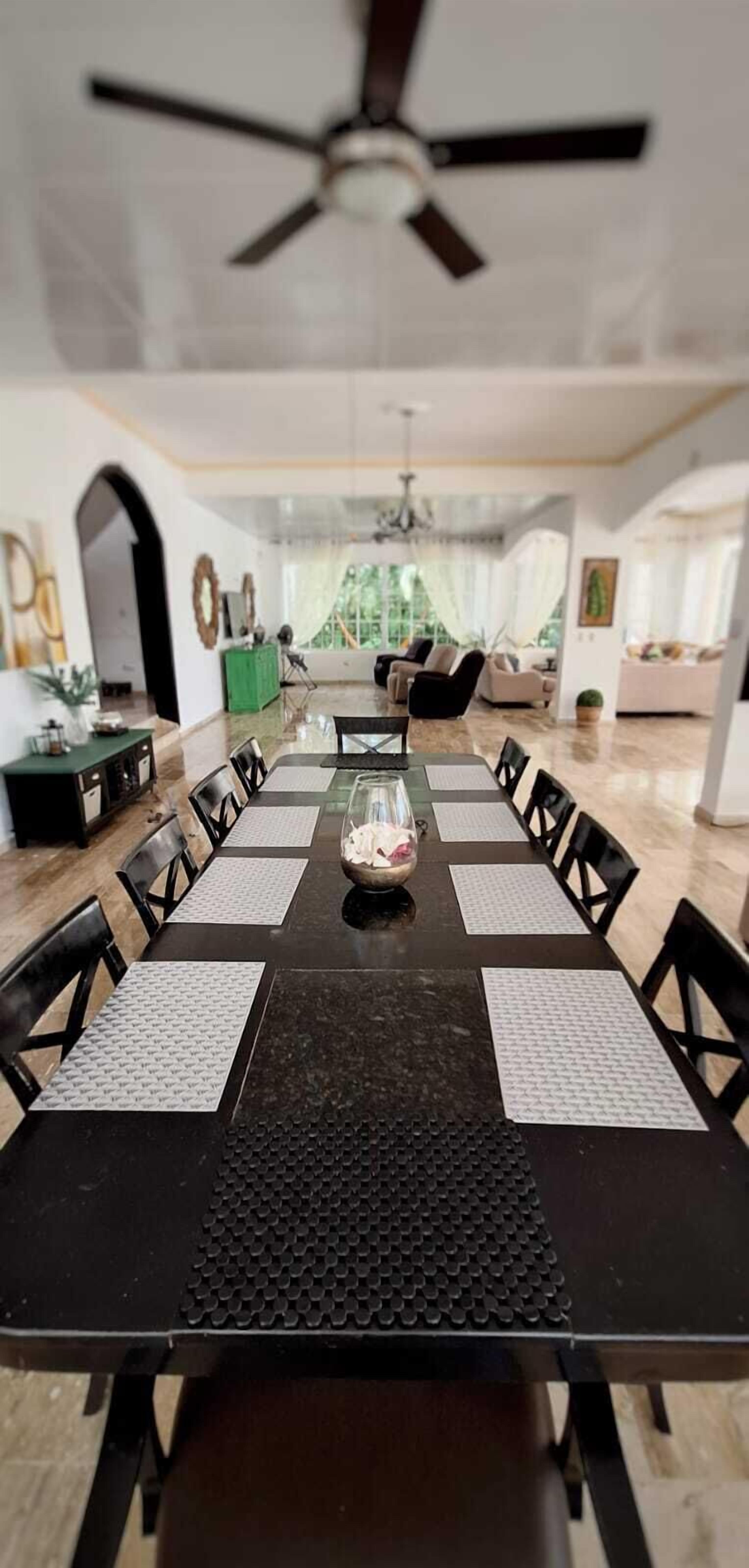 A dining area with a long table, black chairs, and a ceiling fan.