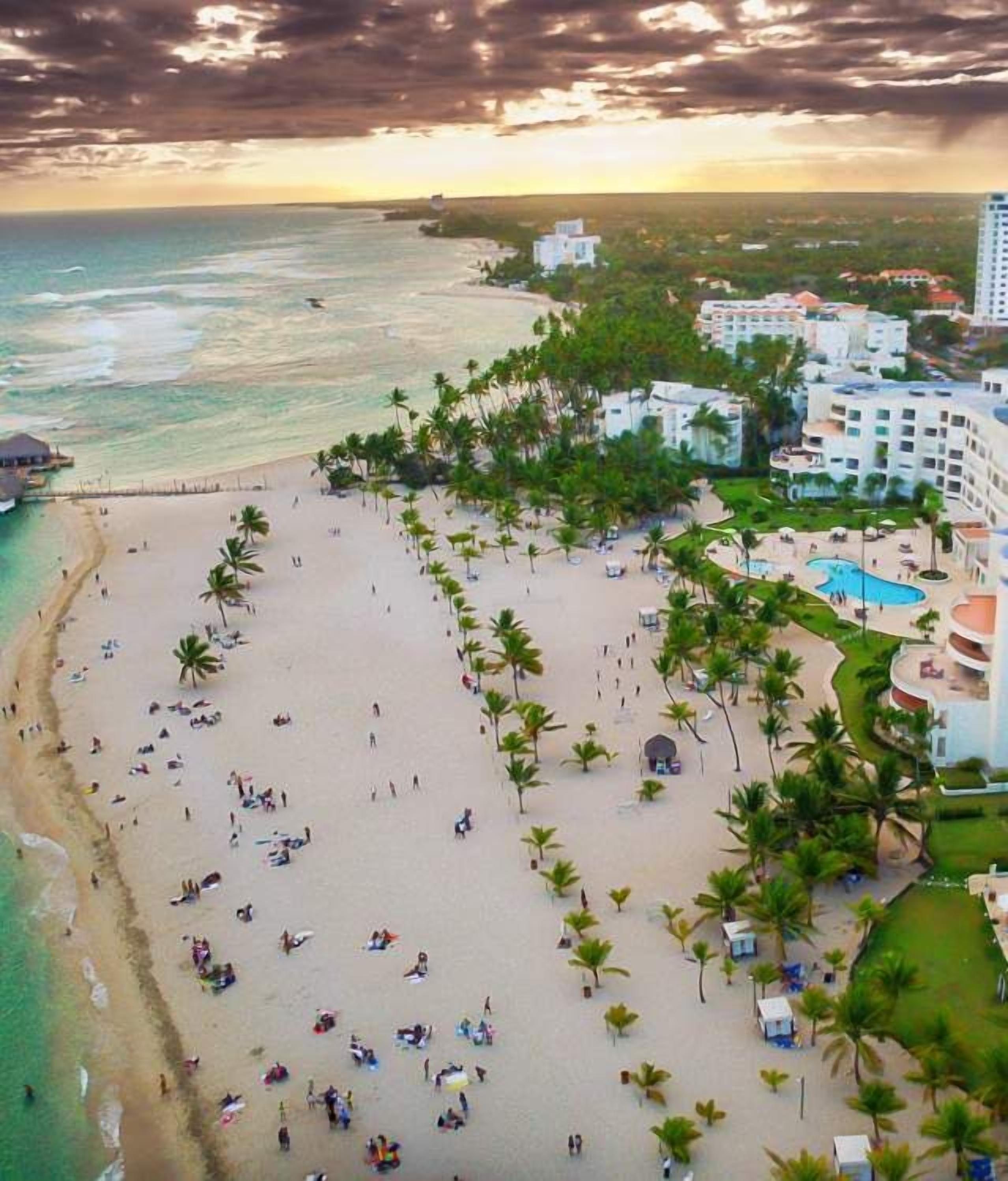 Un complejo turístico en la playa con una extensa playa de arena, palmeras y una zona de piscina.