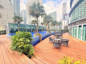 A rooftop terrace with a pool, seating area, and modern buildings in the background. - Vortex suites klcc (Kuala Lumpur)