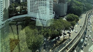 Un edificio de gran altura con una torre distintiva, rodeado por otros rascacielos y una autopista con mucho tráfico.