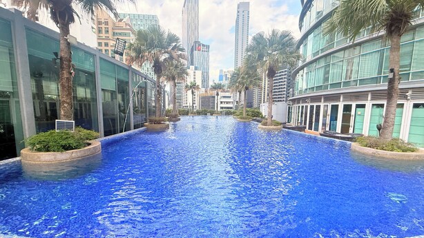 Una piscina con borde de azulejos, rodeada de palmeras y edificios modernos.