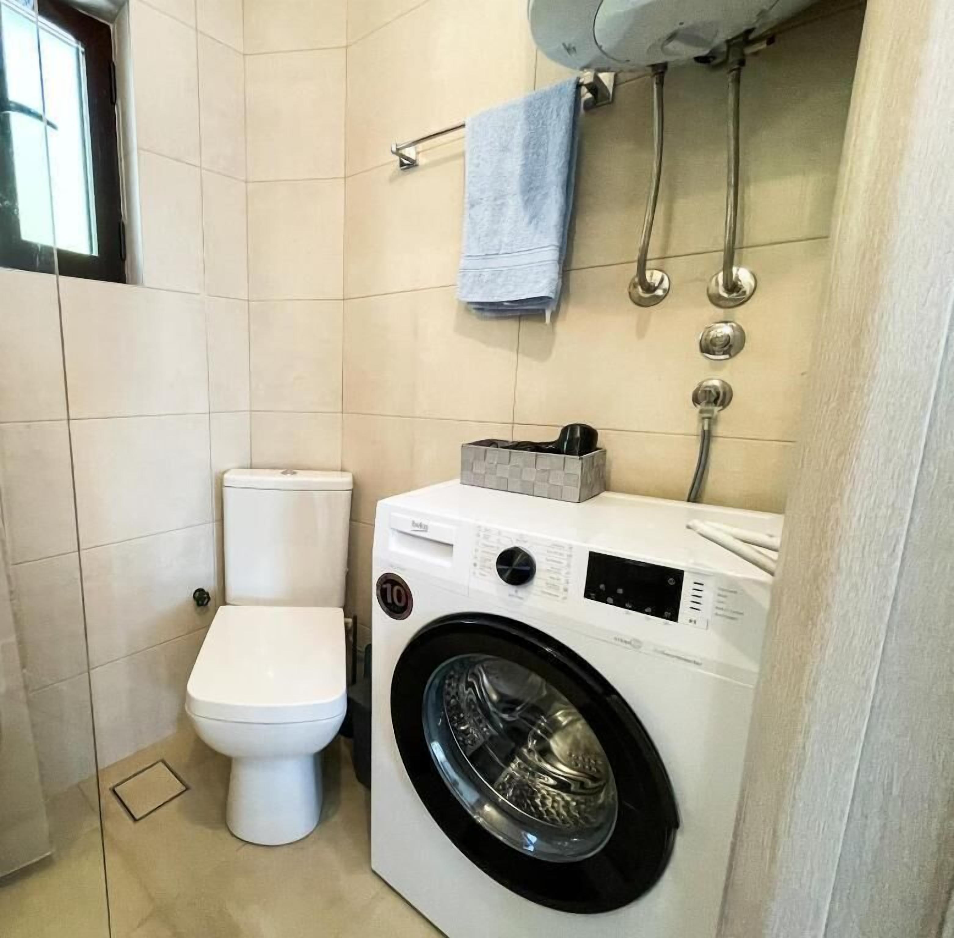 A compact bathroom with a toilet, washing machine, and a towel rack.