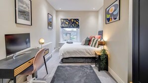 A bedroom with a bed, bedside table, lamp, TV, desk, chair, and a window with a view. - Cosy Walkers Retreat in Meltham Doggie Friendly (Holmfirth)