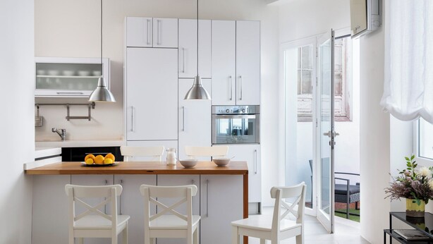 A modern kitchen with white cabinetry, a wooden countertop, and a dining area with white chairs. - Bon voyage home, private patio (Sevilla)