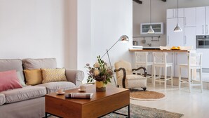 A modern living room with a sofa, coffee table, and a dining area with chairs and a kitchen in the background. - Bon voyage home, private patio (Sevilla)