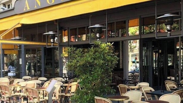 An outdoor cafe with wicker chairs and tables, a yellow awning, and a large window display. - The Poet - Bright and Spacious by Mon Petit Faré (Paris)