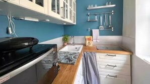 A compact kitchen with white cabinets, a black stove, a sink, and a blue wall.
