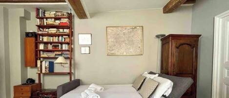 A bedroom with a large bed, a wooden bookshelf, a framed map on the wall, and a wooden cabinet.