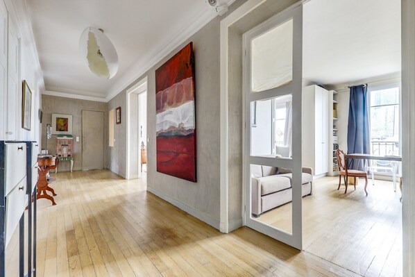 Un salón amplio con suelo de madera, un cuadro abstracto de gran tamaño, un sofá blanco y una zona de comedor con mesa y sillas.