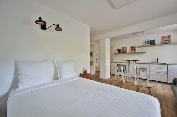 A modern hotel room with a large bed, a small desk, and a kitchenette.