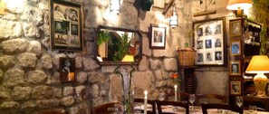 Enjoy a warm and inviting dining experience in this cozy space, complete with a stone wall backdrop, framed photographs, and a beautifully set table.