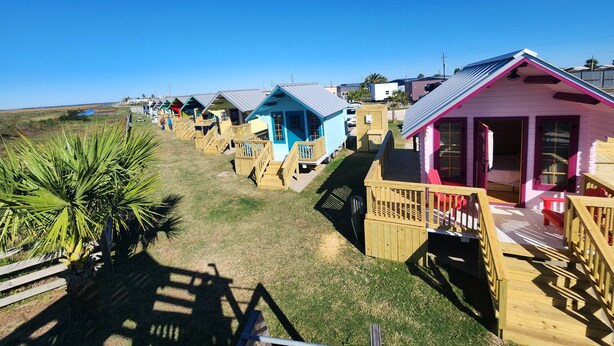 Een rij kleurrijke strandhuisjes met houten terrassen en hekwerk, elk met een eigen kleur.