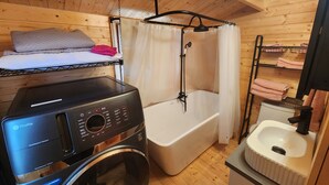 Een kleine kamer met een wasmachine, een badkuip en een klein wastafeltje.