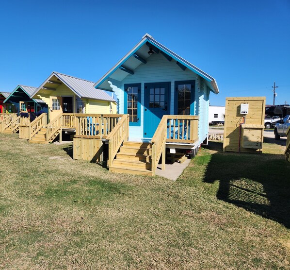 A row of small, colorful cabins with wooden decks and stairs leading to the entrance. - "Ken" Beach Bunkie tiny home, Ken Bunkie beach glamping cabin (Bolivar Peninsula)