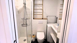 Bathroom features a glass-enclosed shower, white toilet, and wooden shelf above the sink.