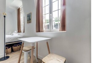 Cozy retreat with a single bed, desk, and stool, featuring a large window and floor lamp.