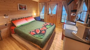 Camera da letto in una baita di legno, con un letto, un comodino, una scrivania e una finestra con tende.