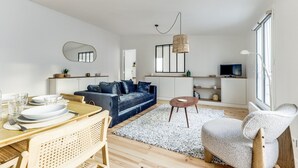A modern living room with a blue sofa, a dining area with a wooden table, and a kitchen area with a TV and shelves. - The Sparkle - Tour Eifflel view by Mon Petit Faré (Paris)