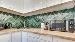 Una cocina moderna con armarios blancos, salpicadero de baldosas verdes en patrón de espiga y un microondas.