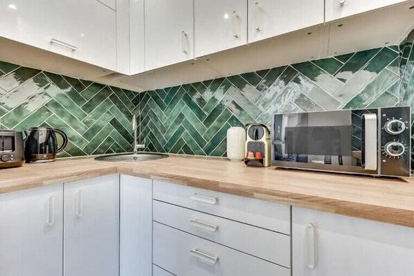A modern kitchen with white cabinets, a herringbone green tile backsplash, and a microwave.