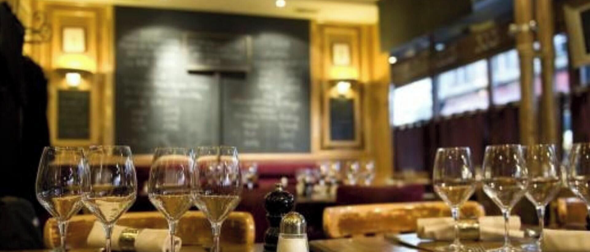 Interior de restaurante con mesas dispuestas para comer, copas de vino y un menú en una pizarra.
