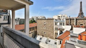 En balkon med udsigt til Eiffeltårnet, bygningsværker i sten og røde tegltage.