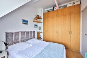 A bedroom with a bed, wooden wardrobe, and a small shelf with books.