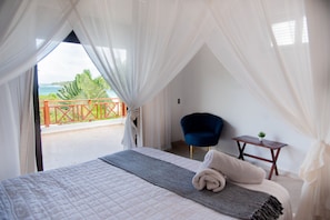 A bedroom with a bed, a chair, a small table, and a balcony with a railing.