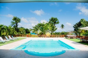 A swimming pool with a wooden deck, surrounded by lush greenery and palm trees. - Villa Bahia Rincon: A Taste of Paradise (Samaná Province)