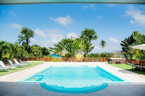 A swimming pool with a wooden deck, surrounded by lush greenery and palm trees.