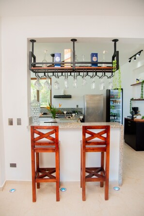 A kitchen with a bar area, two wooden bar stools, a hanging light fixture, and a refrigerator. - Villa Bahia Rincon: A Taste of Paradise (Samaná Province)