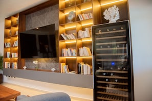 A modern living room with a large flat-screen TV mounted on a wooden wall, surrounded by shelves with books and decorative items.
