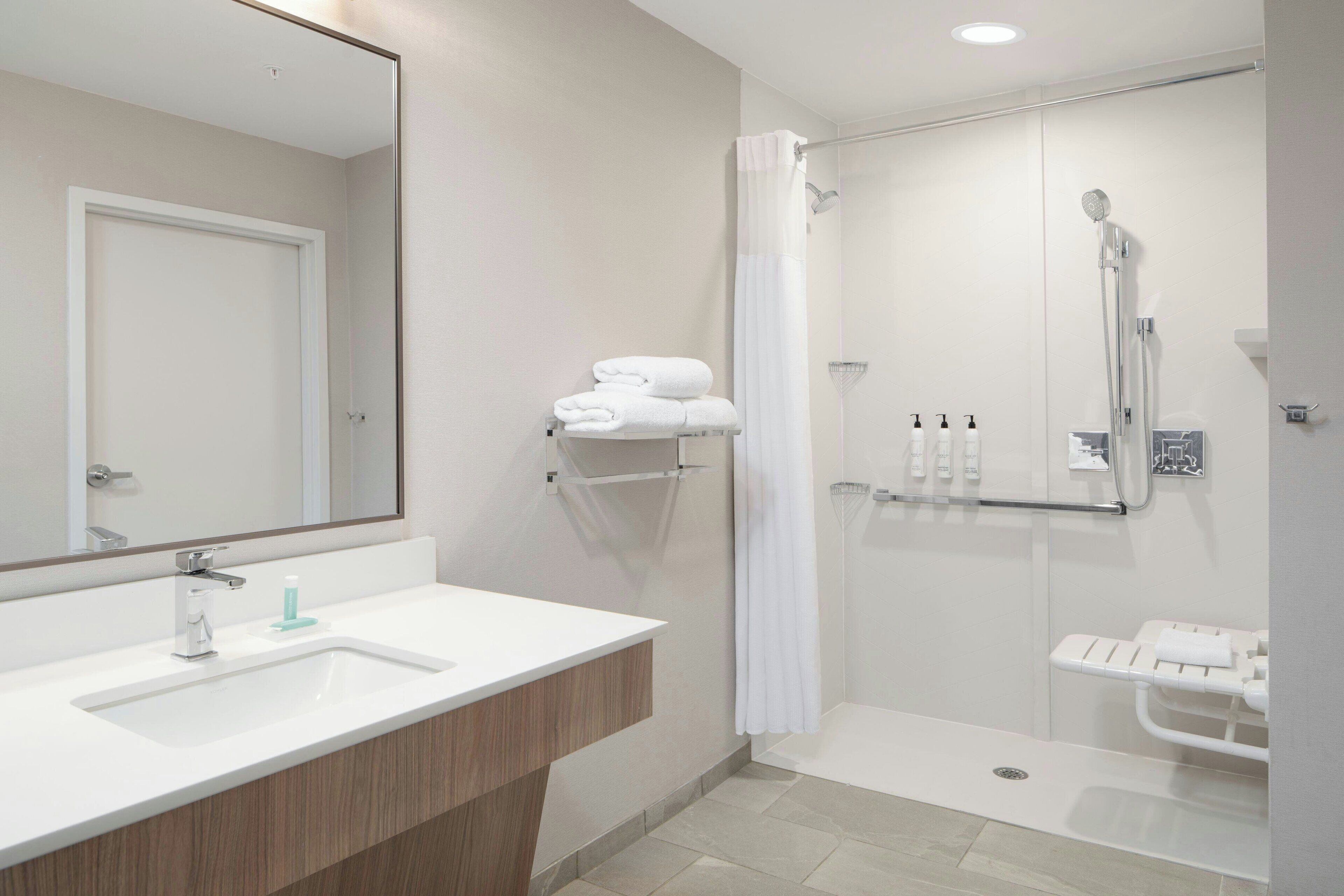 A modern bathroom with a white sink, mirror, and shower area.
