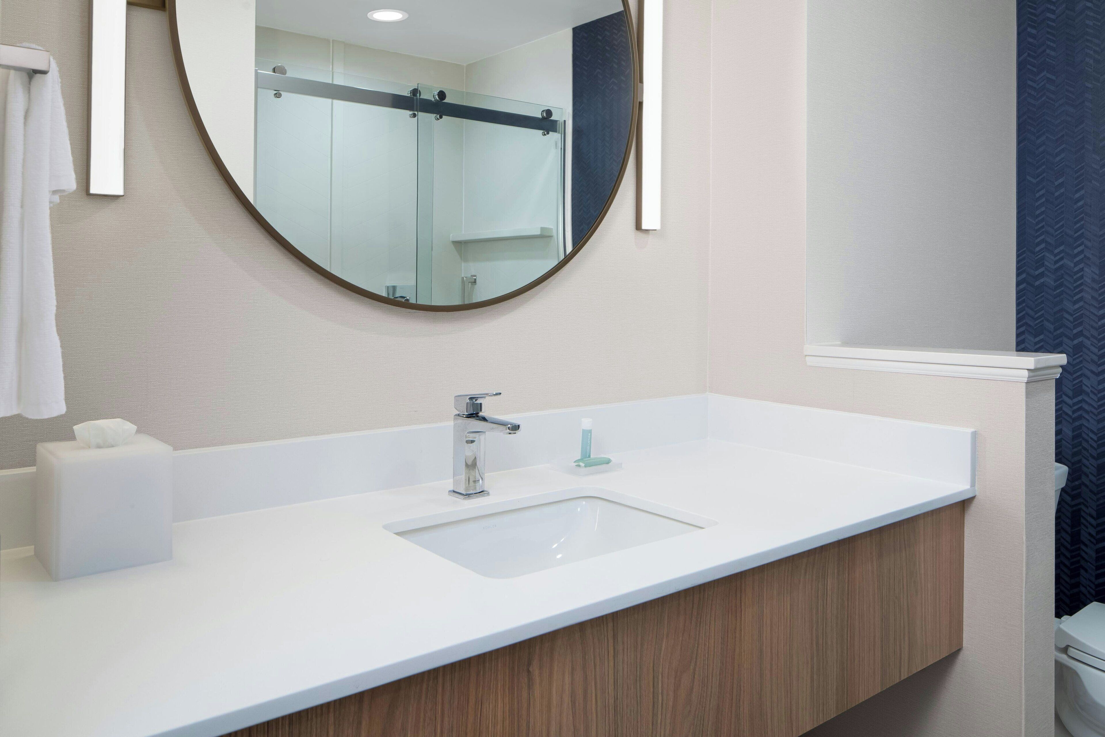 Une salle de bain avec un lavabo blanc, un miroir rond et un porte-serviettes.