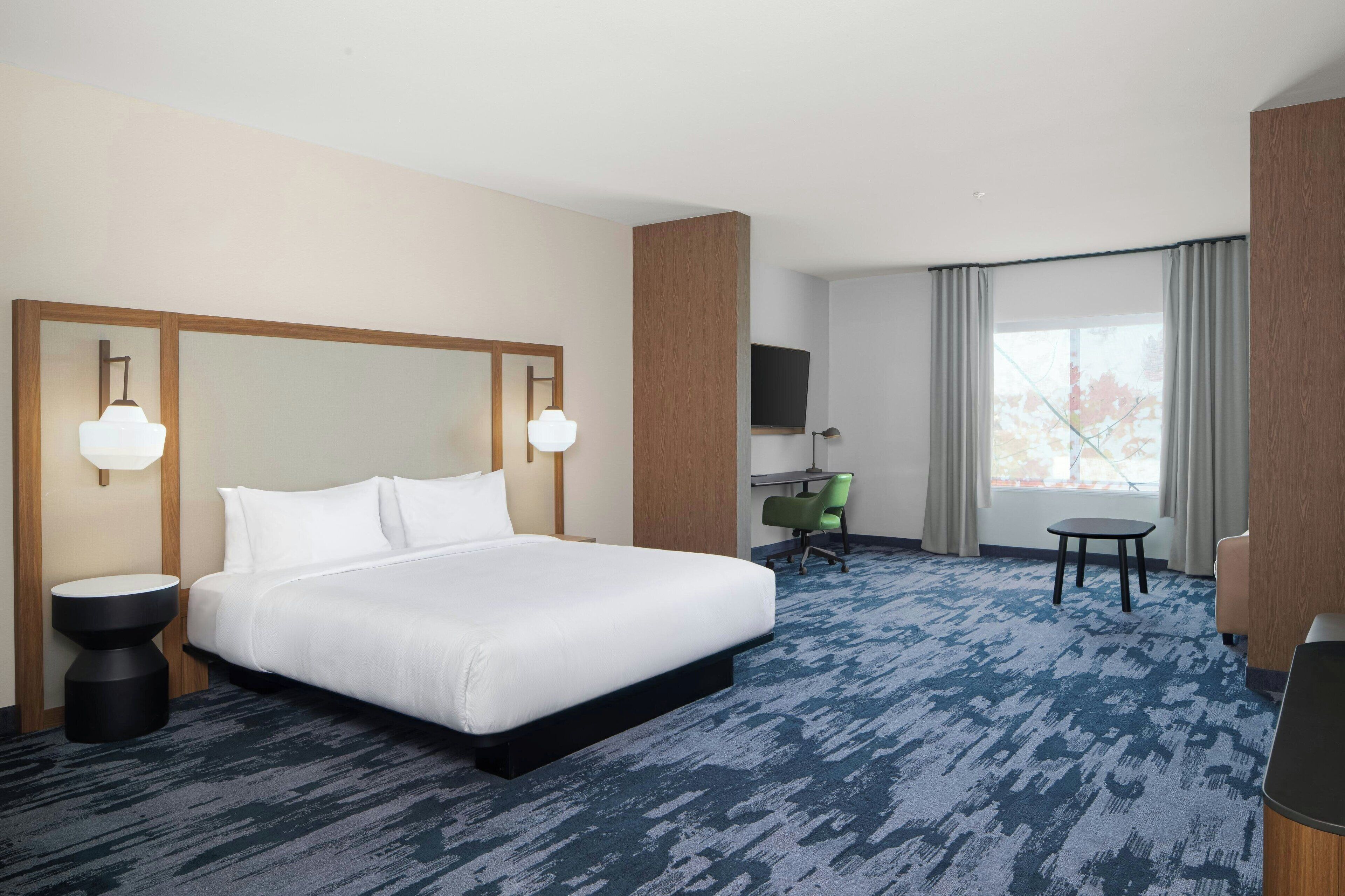 Habitación de hotel con una cama grande, un escritorio, una silla y un televisor.