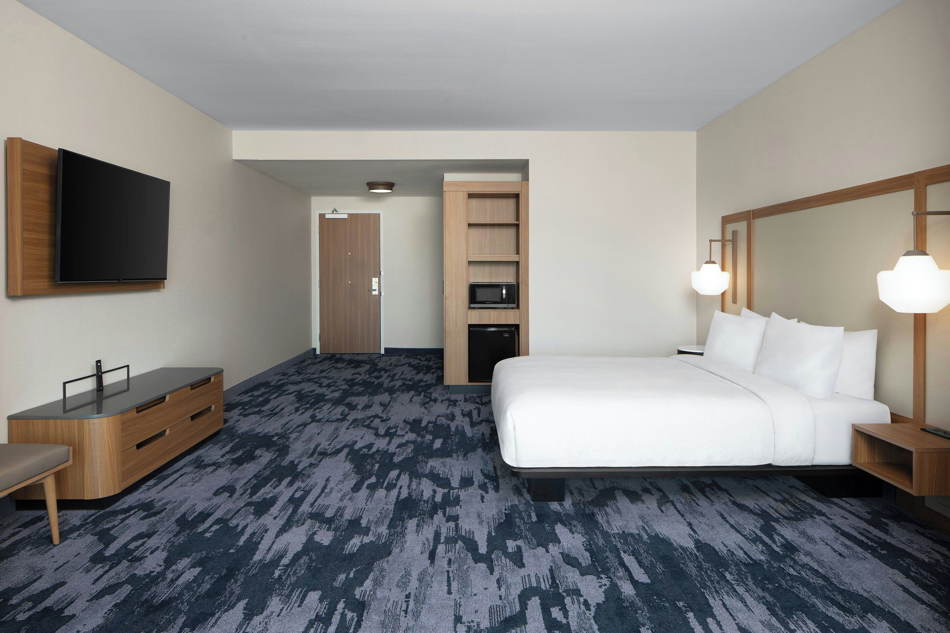Ein Hotelzimmer mit Bett, Wandfernseher, Schreibtisch mit Schubladen, Mikrowelle und Kleiderschrank.