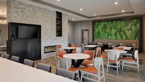 A modern dining area with round tables and orange chairs, a flat-screen TV mounted on a brick wall, and a green patterned wall in the background. - Residence Inn by Marriott Huntsville - Madison (Madison)