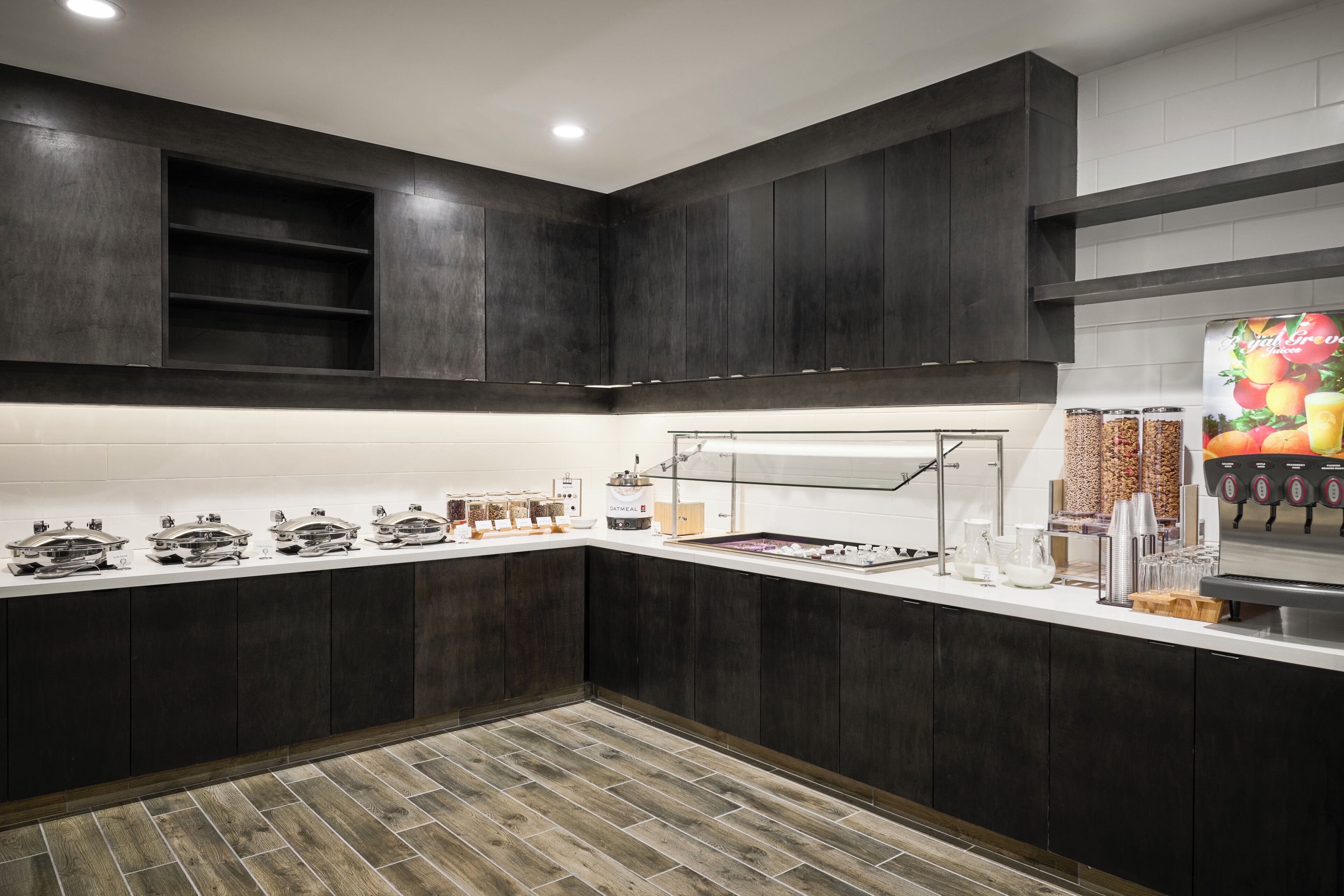 A modern kitchen with dark cabinetry, a white countertop, and a coffee station.