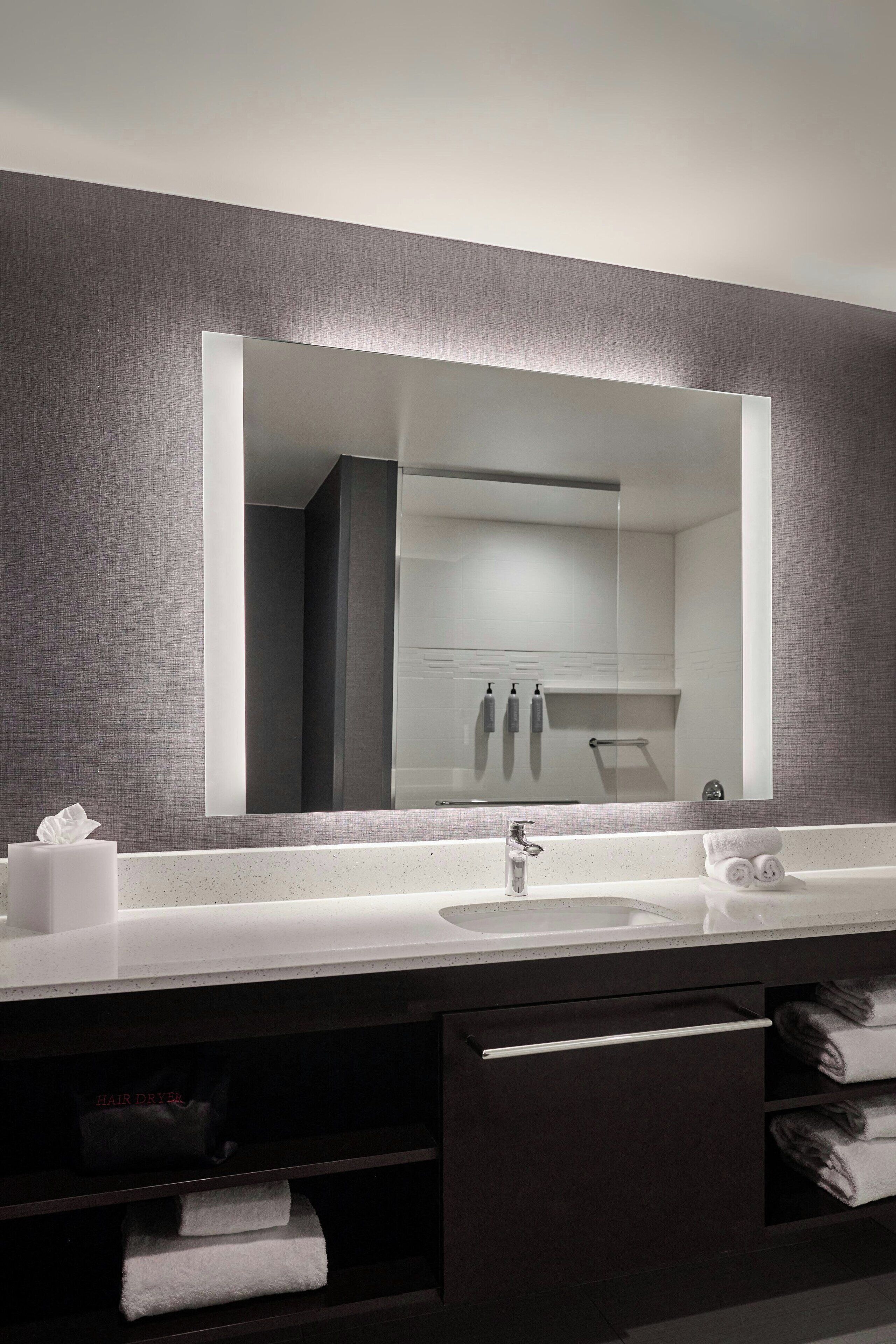A modern bathroom with a large mirror, a white sink, and dark cabinetry.