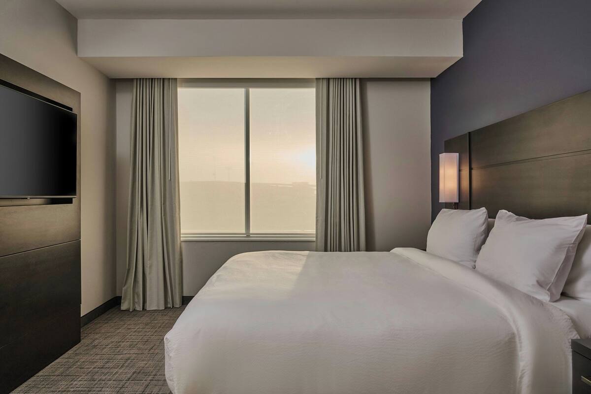 Una habitación de hotel con una cama grande, un televisor de pantalla plana en la pared y una ventana con cortinas.