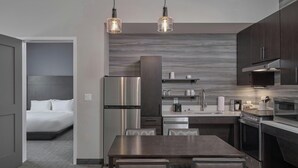 A modern kitchen with stainless steel appliances, a dining area with a table and chairs, and a bedroom visible through an open door. - Residence Inn by Marriott Huntsville - Madison (Madison)