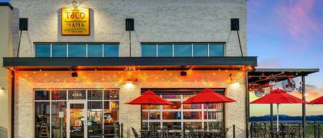 A restaurant with a brick facade, outdoor seating with red umbrellas, and a sign reading "Taco Mama".