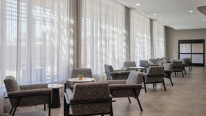 A spacious hotel lobby with rows of armchairs and small tables, large windows with sheer curtains, and a modern ceiling design. - Courtyard by Marriott Huntsville-Madison (Madison)