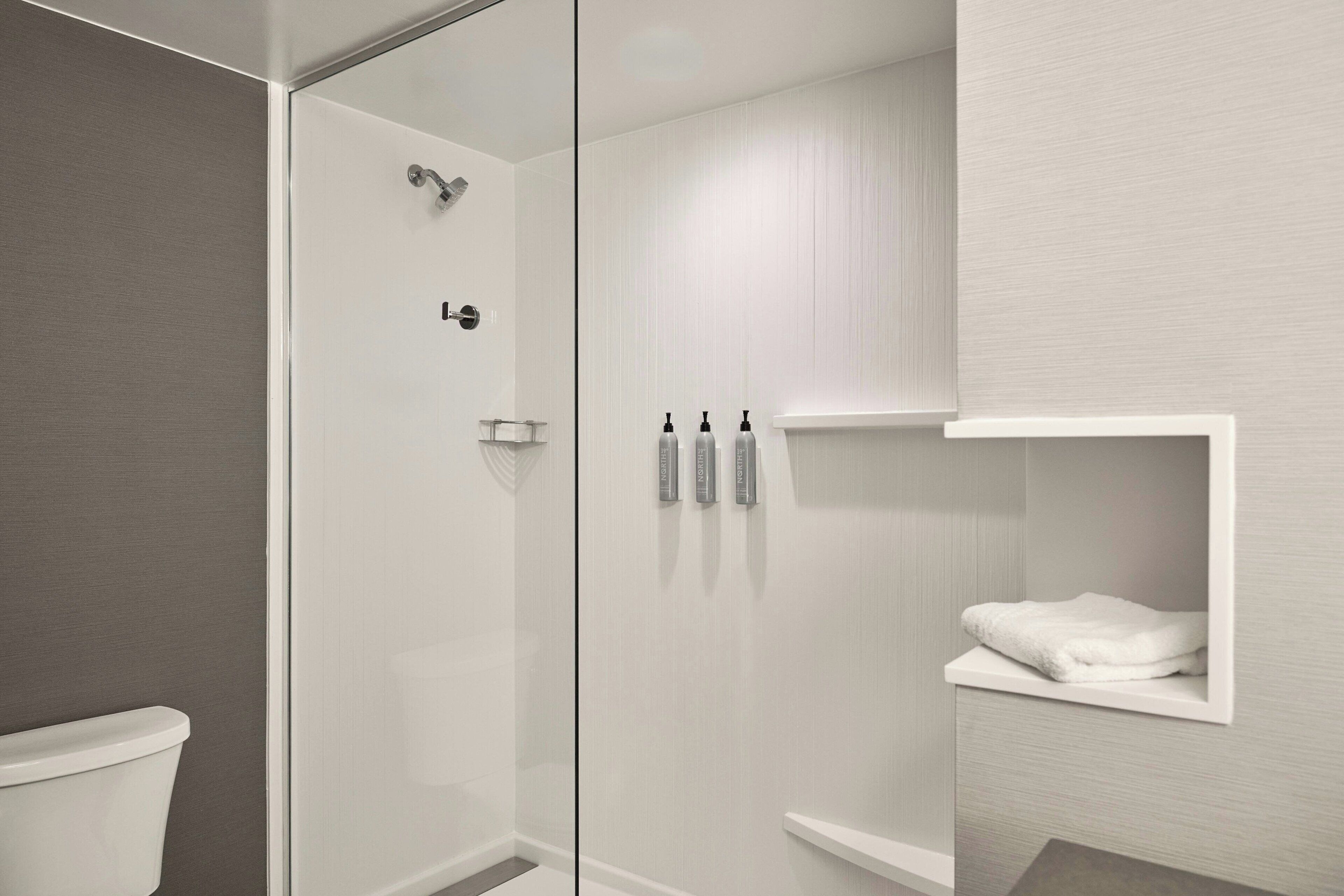 Une salle de bain moderne avec une douche à parois de verre, des toilettes et une étagère à serviettes.