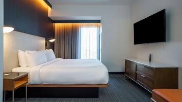 A modern hotel room with a large bed, a flat-screen TV, a desk, and a dresser.