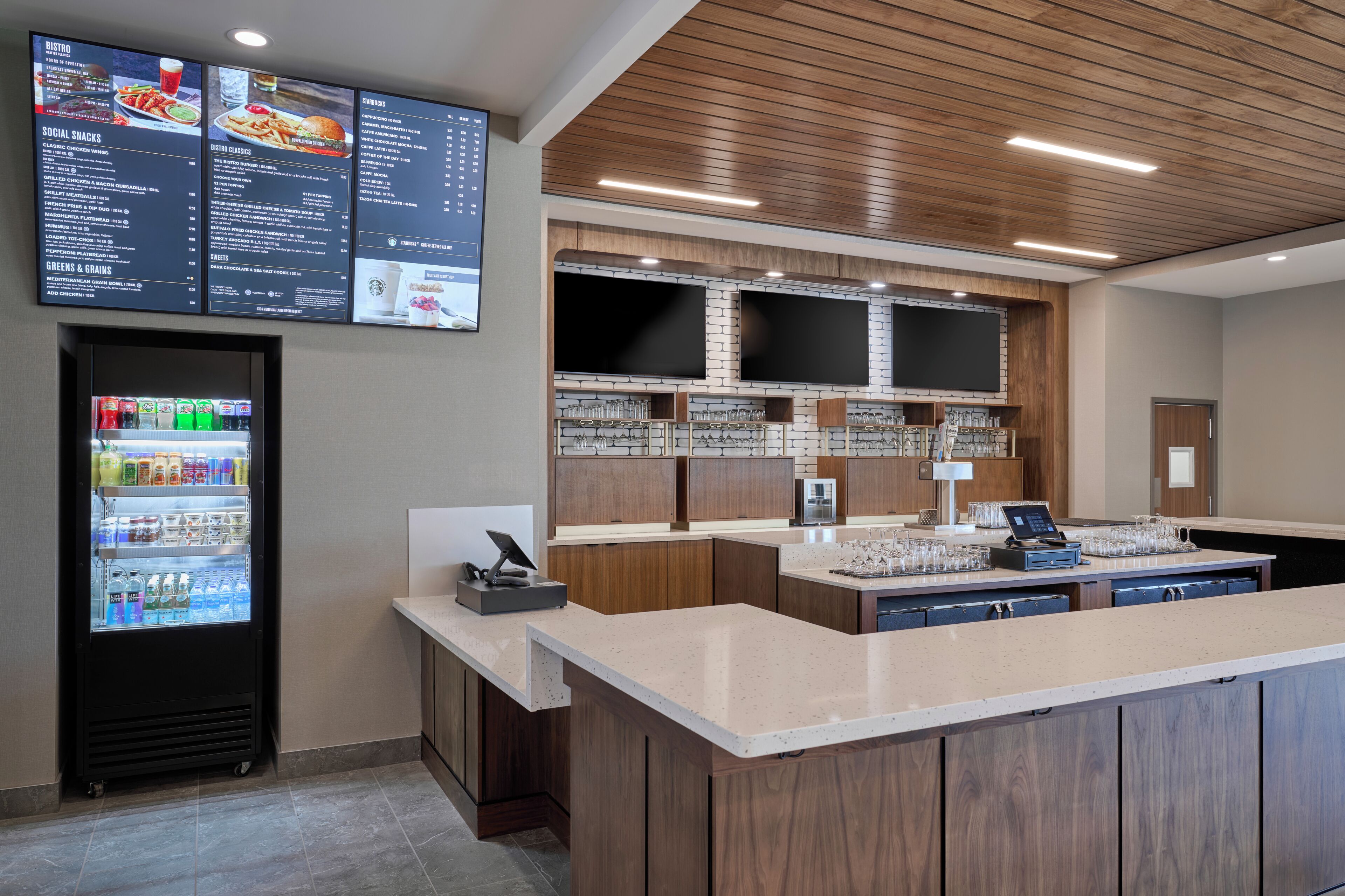 A modern restaurant with a menu board, a beverage dispenser, and a bar area.