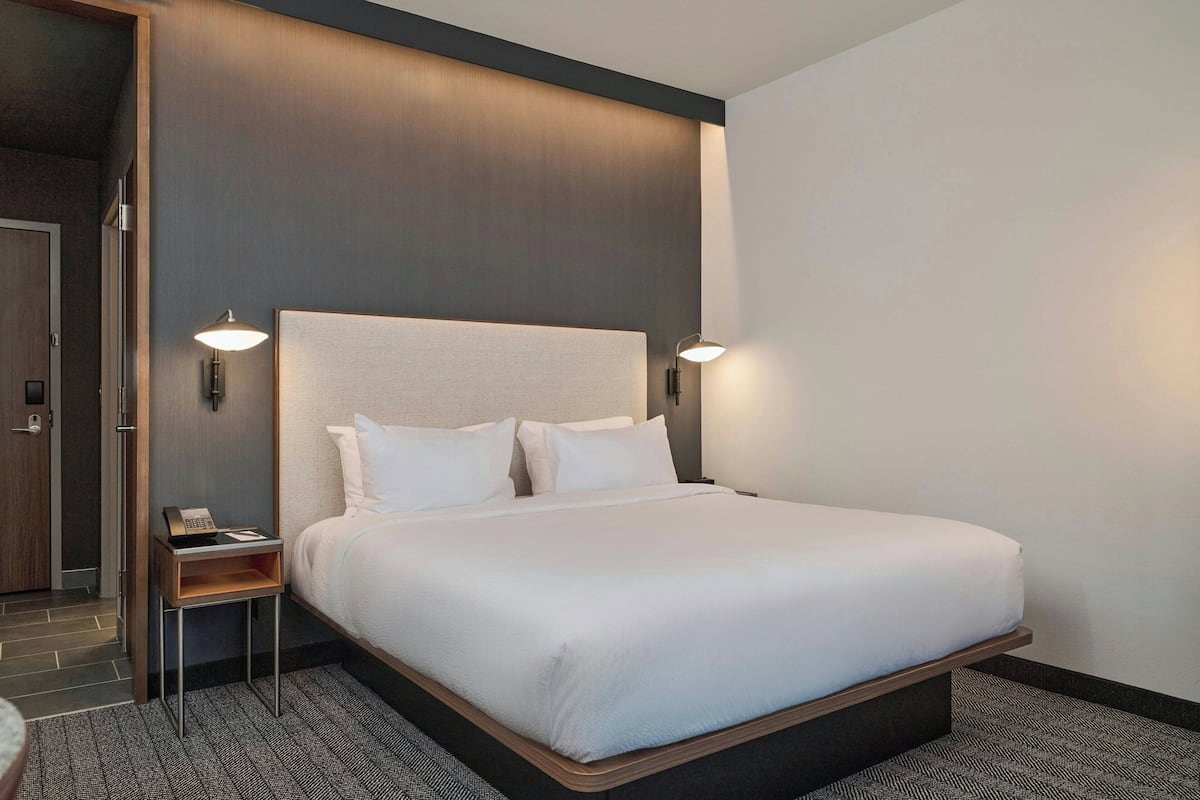 A hotel room with a large bed, two bedside tables, a nightstand, and a wall-mounted phone.